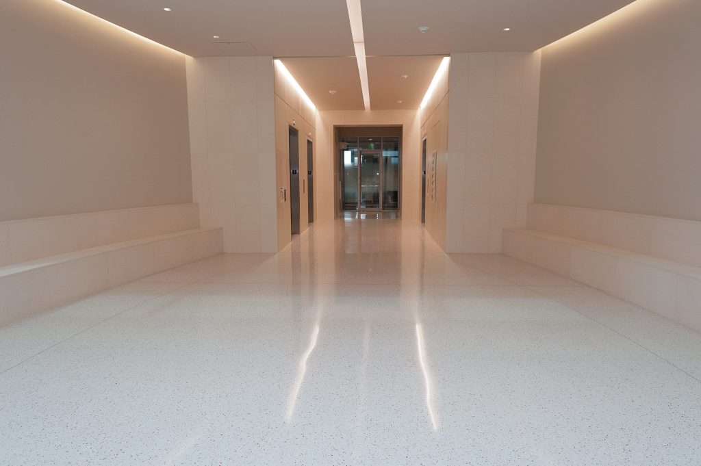 Image of a long hallway with dim yellow lights and two glass doors at the end.