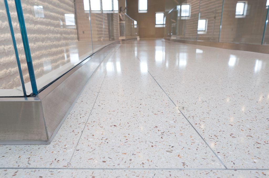 Close up image of a glossy white speckled floor with the silver and glass siding showing on the left.