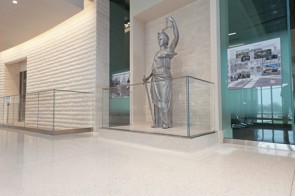Image of a glossy white speckled floor and a silver statue inside of a glass wall covering half of their body.